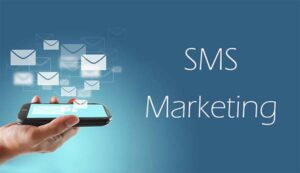 A hand holding a smartphone with multiple email icons floating above the screen, with the text SMS Marketing to the right. A hand holding a smartphone with multiple email icons floating above the screen, with the text SMS Marketing to the right.